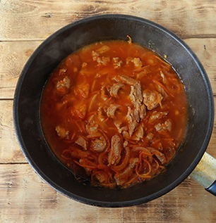 Schweinefleischstücke mit Soße in einer Pfanne