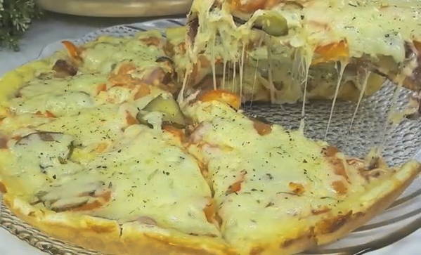 Pizza mit Essiggurken, Wurst und Käse in einer Pfanne